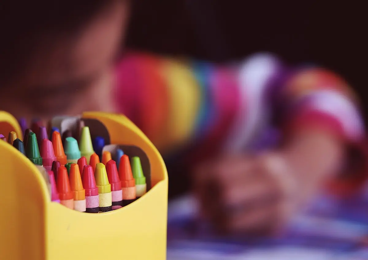 A child colouring with a box of crayons